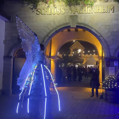 Ein festlich beleuchteter Eingang zum Schloss Wachenheim. Vor dem Tor steht eine Person in einem leuchtenden Kostüm.