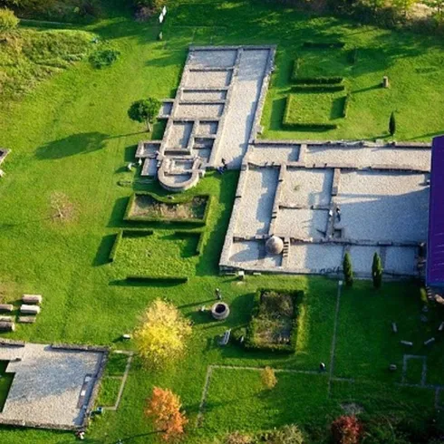 Eine Luftaufnahme von historischen Ruinen in einer grünen Landschaft. Die Strukturen sind klar sichtbar und von Bäumen umgeben.
