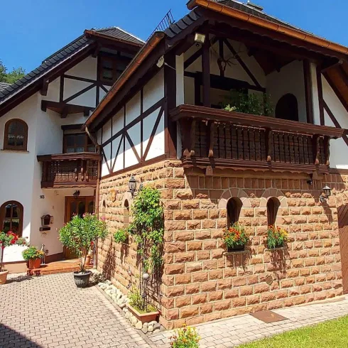 Ein charmantes Haus mit Fachwerk-Architektur und einem schönen Garten. Die sonnige Umgebung und die klare blaue Himmel verleihen dem Bild eine einladende Atmosphäre.