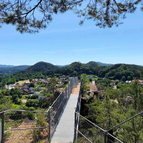 Eine Hängebrücke übergrünt das Tal mit Hügeln im Hintergrund. Der klare Himmel sorgt für eine schöne Aussicht auf die Umgebung.