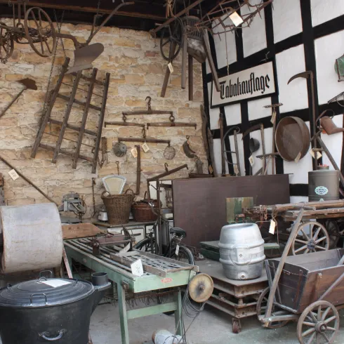 Ein historischer Geräteschuppen mit verschiedenen landwirtschaftlichen Werkzeugen und Maschinen. Die Wände sind mit alten Werkzeugen dekoriert, die die ländliche Vergangenheit zeigen.