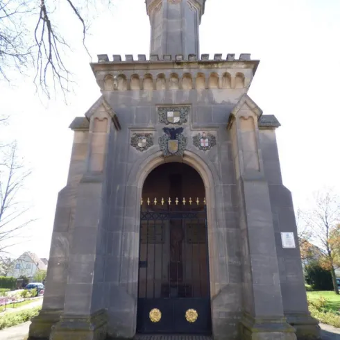 Ein historisches Mausoleum mit einer beeindruckenden Fassade aus Stein. Die große, verzierte Tür und der hohe Turm verleihen ihm eine markante Ausstrahlung.