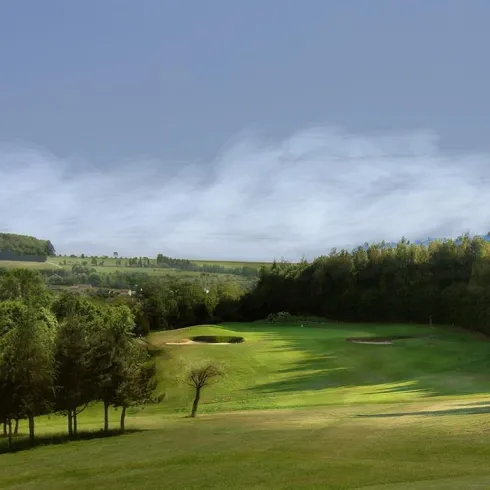 Ein malerischer Golfplatz mit grünem Rasen und sanften Hügeln. Im Hintergrund sind Bäume und ein klarer Himmel sichtbar.