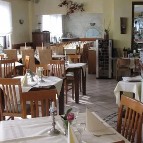 Ein einladendes Restaurant mit Holztischen und Stühlen. Die Tische sind elegant gedeckt und der Raum ist hell und freundlich.