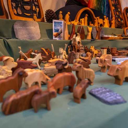 Eine Vielzahl von handgefertigten Holzfiguren ist auf einem Tisch ausgestellt. Die Figuren repräsentieren verschiedene Tiere und kunstvolle Designs.