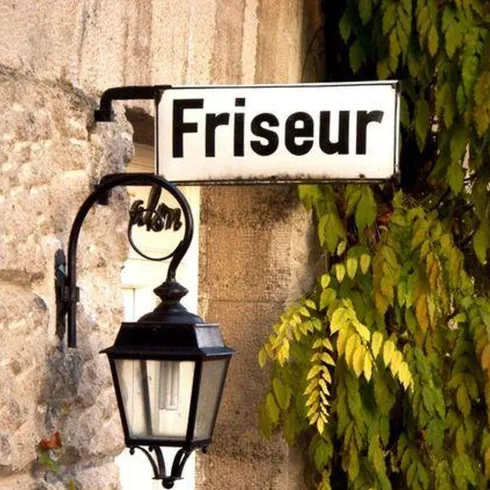 Eine Hauswand mit einem Schild, auf dem Schild steht "Friseur" geschrieben.