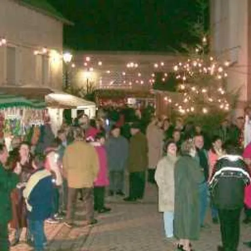 Eine belebte Straße mit Ständen und Lichtern bei Nacht. Viele Menschen genießen das Ambiente und die festliche Atmosphäre.
