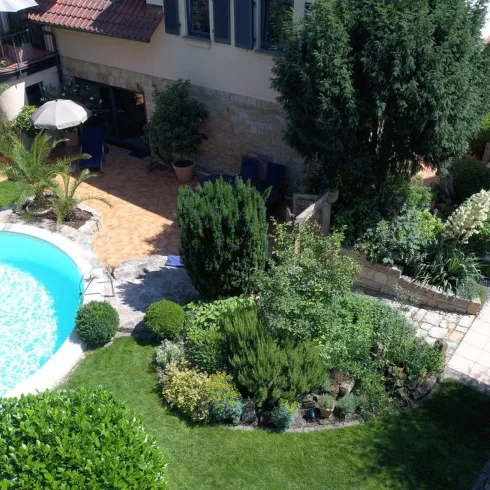 Ein schöner Garten mit einem Pool in der Mitte. Umgeben von üppigem Grün und gemütlichen Sitzbereichen.