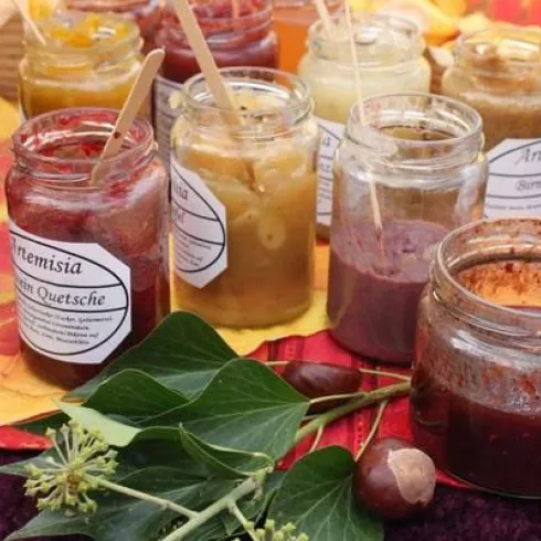 Ein Tisch mit verschiedenen Gläsern voller Marmelade und Chutneys. Die Gläser sind schön beschriftet und umgeben von buntem Herbstdekor.