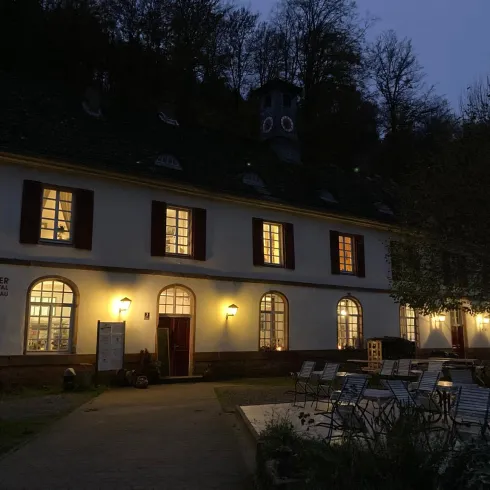 Ein Café in einem historischen Gebäude, beleuchtet im Abendlicht. Umgeben von Bäumen und Stühlen im Freien.