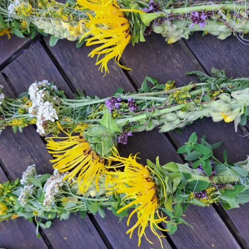 Drei bunte Kräutersträuße liegen auf einem Holztisch. Die Sträuße sind mit verschiedenen Pflanzen und Blumen geschmückt.