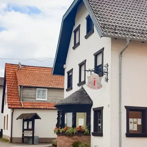 Ein charmantes zweistöckiges Haus mit einem einladenden Eingangsbereich. Die Fassade ist hell und wird von bepflanzten Kästen geschmückt.