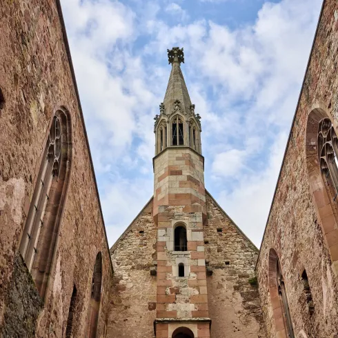 Eine alte Kirche mit einem hohen Turm und historischen Mauern. Der Himmel ist teilweise bewölkt und verleiht der Szene eine ruhige Atmosphäre.