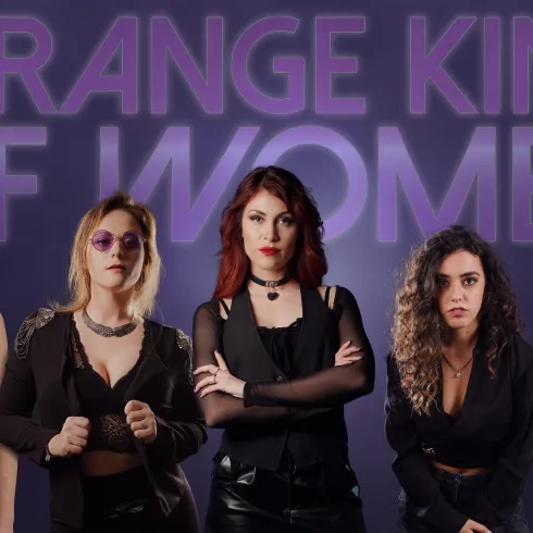 Eine Gruppe von fünf Frauen in stylischen, dunklen Outfits posiert vor einem lila Hintergrund. Der Schriftzug "STRANGE KIND OF WOMEN" steht prominent im Bild.