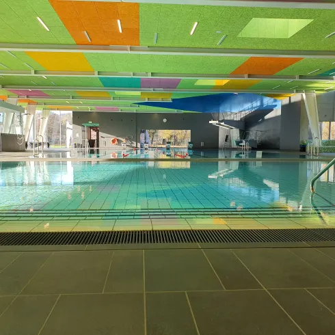 Ein moderner Innenpool mit klarem Wasser und bunten Deckenpaneelen. Die Umgebung ist hell und einladend.