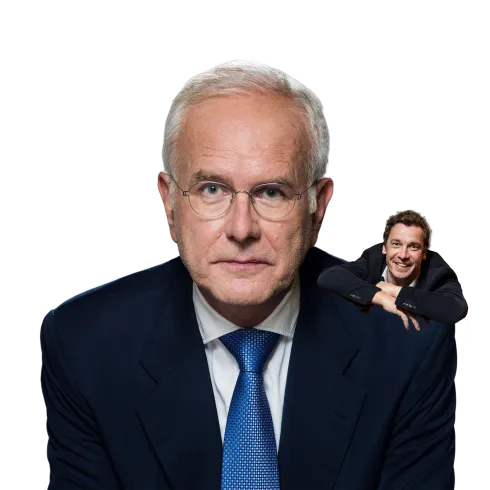 Ein älterer Mann in einem dunklen Anzug mit Brille schaut direkt in die Kamera. Im Hintergrund ist ein jüngerer Mann zu sehen, der entspannt wirkt.