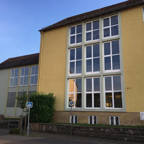 Ein modernes Gebäude mit großen Fenstern in einer ruhigen Umgebung. Die Fassade ist gelb und die oberen Etagen sind hell und einladend.