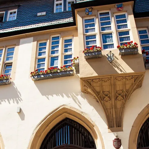 Ein historisches Gebäude mit einem schönen Erker und vielen Fenstern. Bunte Blumen schmücken die Fensterbanken.