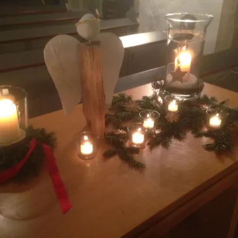 Ein dekorierter Tisch mit Kerzen, einem Holzengel und einer Weihnachtskranz. Die Atmosphäre ist festlich und gemütlich.