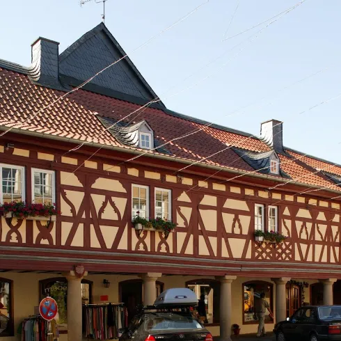 Ein traditionelles Fachwerkhaus mit rot-weißer Fassade. Vor dem Gebäude stehen mehrere Autos und es ist ein klarer Himmel zu sehen.