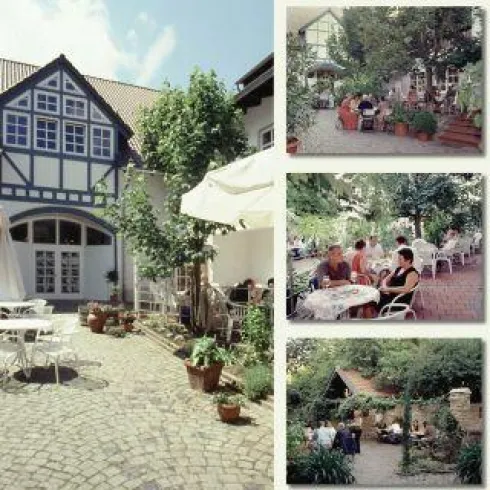 Ein einladender Innenhof mit Pflastersteinen und einem gemütlichen Café. Umgeben von vielen Pflanzen und Gästen, die die Atmosphäre genießen.
