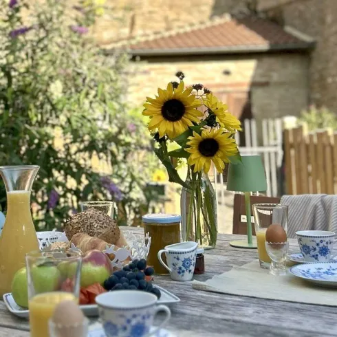 Ein Tisch im Freien, gedeckt mit frischem Obst, Getränken und Geschirr. In der Mitte steht eine Vase mit Sonnenblumen, umgeben von einer schönen, entspannten Atmosphäre.
