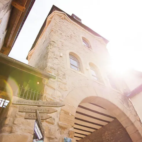 Ein historischer Torbogen aus Stein unter klarem Himmel. Sonnenlicht strahlt durch den Bogen und erhellt die Umgebung.