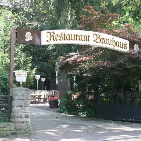 Ein einladender Eingang zu einem Restaurant namens "Brauhaus". Der Bereich ist von Bäumen umgeben und bietet eine angenehme Atmosphäre.