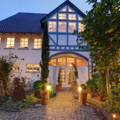 Ein charmantes Haus mit einem schönen Eingangsbereich und warmem Licht in den Fenstern. Umgeben von Pflanzen und Laternen, strahlt es eine einladende Atmosphäre aus.