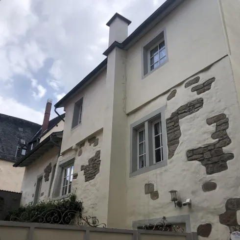 Ein altes, charmantes Haus mit einem hellen Putz und einigen unregelmäßigen Steinelementen. Der Himmel ist teilweise bewölkt, was dem Bild eine stimmungsvolle Atmosphäre verleiht.