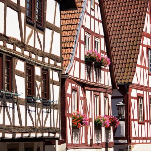 Eine malerische Straßenszene mit Fachwerkhäusern und bunten Blumenbalkonen. Die Kombination aus Weiß und Rot verleiht der Architektur einen charmanten Charakter.