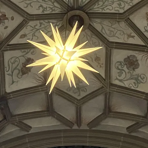 Eine leuchtende Sternenlampe hängt unter einer kunstvoll verzierten Decke. Die Decke zeigt florale Motive und geometrische Muster.