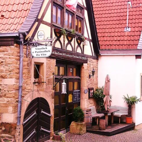 Ein charmantes Fachwerkhaus mit Blumen und einer italienischen Flagge. Es gibt eine gemütliche Sitzecke vor dem Eingang.