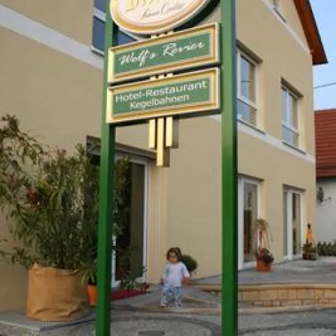 Ein großes Schild vor einem Gebäude zeigt den Namen und die Dienstleistungen eines Hotels und Restaurants an. Ein kleines Kind spielt in der Nähe des Eingangs.