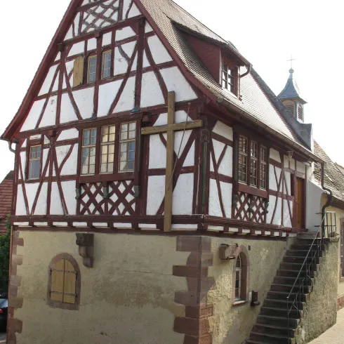 Ein traditionelles Fachwerkhaus mit einem charakteristischen rot-weißen Design. Es hat eine steinerne Basis und eine Treppe, die zum Eingang führt.