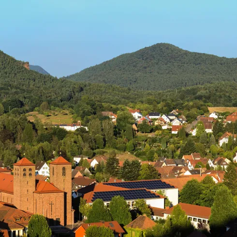 Eine malerische Stadt im Tal, umgeben von grünen Hügeln und Bergen. Im Vordergrund sind historische Gebäude und moderne Häuser zu sehen.