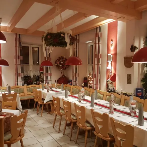 Ein gemütliches Restaurant mit langen Tischen und Holzbänken. Rote Lampen hängen von der Decke, und die Wände sind festlich dekoriert.