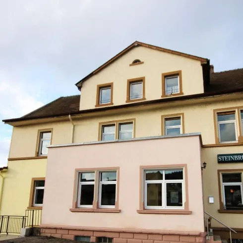 Ein zweigeschossiges Gebäude mit einer hellen Fassade. Das Café ist gut sichtbar mit einem Schild über dem Eingang.