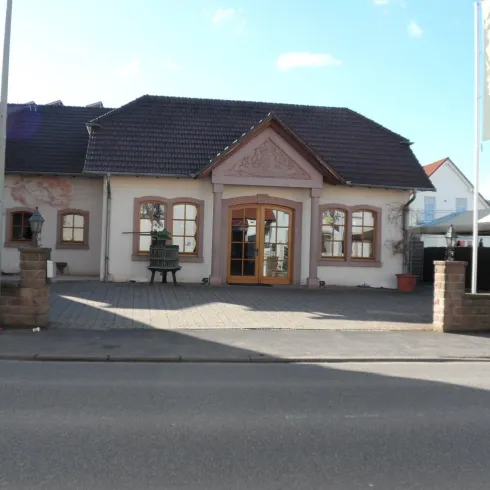 Ein gemütliches Gebäude mit einer einladenden Eingangstür. Umgeben von einem gepflasterten Vorplatz und einer ruhigen Straße.