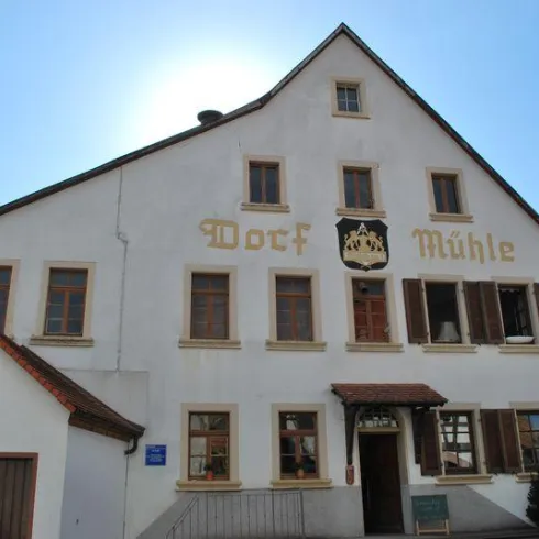 Ein traditionelles Gebäude mit der Aufschrift "Dorf Mühle". Es hat große Fenster und eine einladende Fassade.