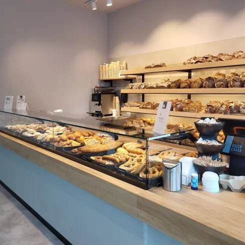 Eine Bäckerei mit einer Vielzahl von frischen Brötchen und Gebäck auf einem Tisch. Im Hintergrund sind Regale mit weiteren Backwaren zu sehen.
