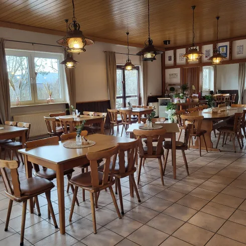 Ein gemütliches Restaurant mit vielen Holztischen und Stühlen. Die Fenster lassen viel Tageslicht herein und sorgen für eine einladende Atmosphäre.