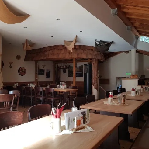 Ein gemütliches Restaurant mit Holzmöbeln und einem hellen Raum. Die Tische sind dekoriert und es gibt eine einladende Atmosphäre.