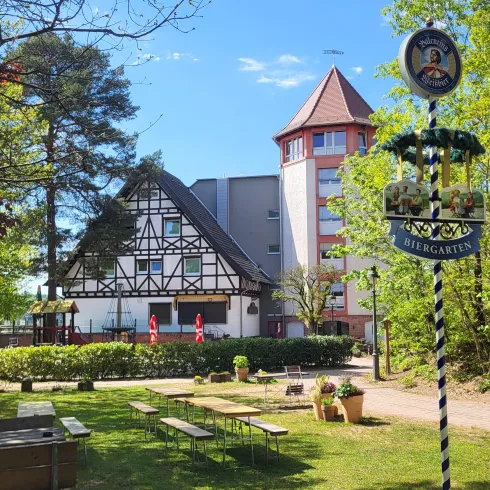 Ein einladendes Gebäude im ländlichen Stil, umgeben von Bäumen und grünem Gras. Ein Schild mit der Aufschrift "Biergarten" steht im Vordergrund.
