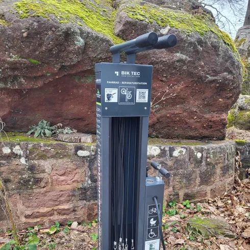 Eine Fahrrad-Reparaturstation mit verschiedenen Werkzeugen. Sie steht in einer natürlichen Umgebung zwischen Steinen und Laub.