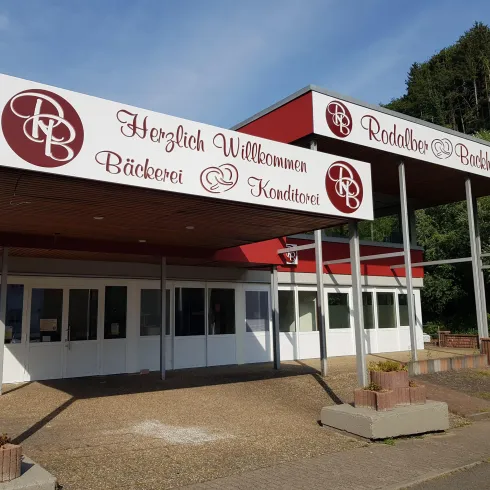Ein Bäckerei- und Konditoreigeschäft mit einem einladenden Eingang. Das Schild weist auf frische Backwaren und süße Leckereien hin.