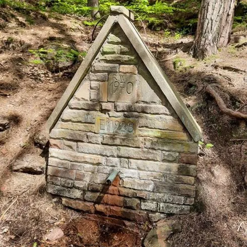 Ein kleines aus Stein gebautes Haus mitten im Wald, umgeben von Bäumen.