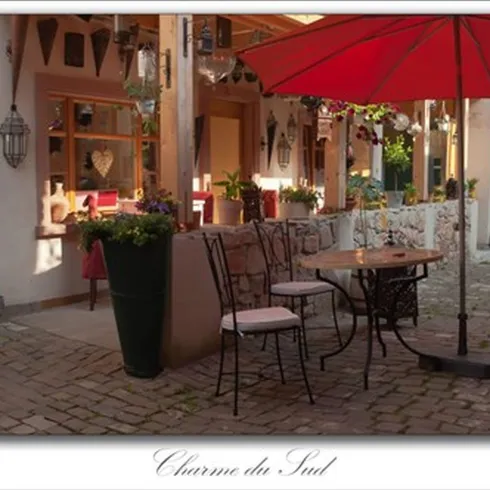 Ein gepflasterter, schön dekorierter Innenhof. der Innenhof ist Bestuhlt und einSchirm steht an dem Tisch.Das Ganze ist der Innenhof des Cafe Charme du Sud.