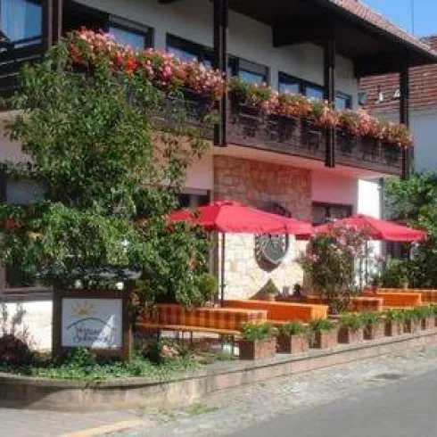 Die Außenansicht des Weinhauses Zeigt eine Terasse mit Bierbänken.