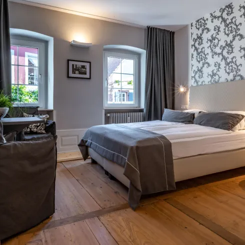Ein modernes Schlafzimmer mit einem großen Bett und elegantem Dekor. Die Wände haben ein schönes Muster und große Fenster sorgen für viel Tageslicht.